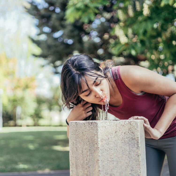 Eine Frau trinkt in einem Park aus einen Trinkbrunnen